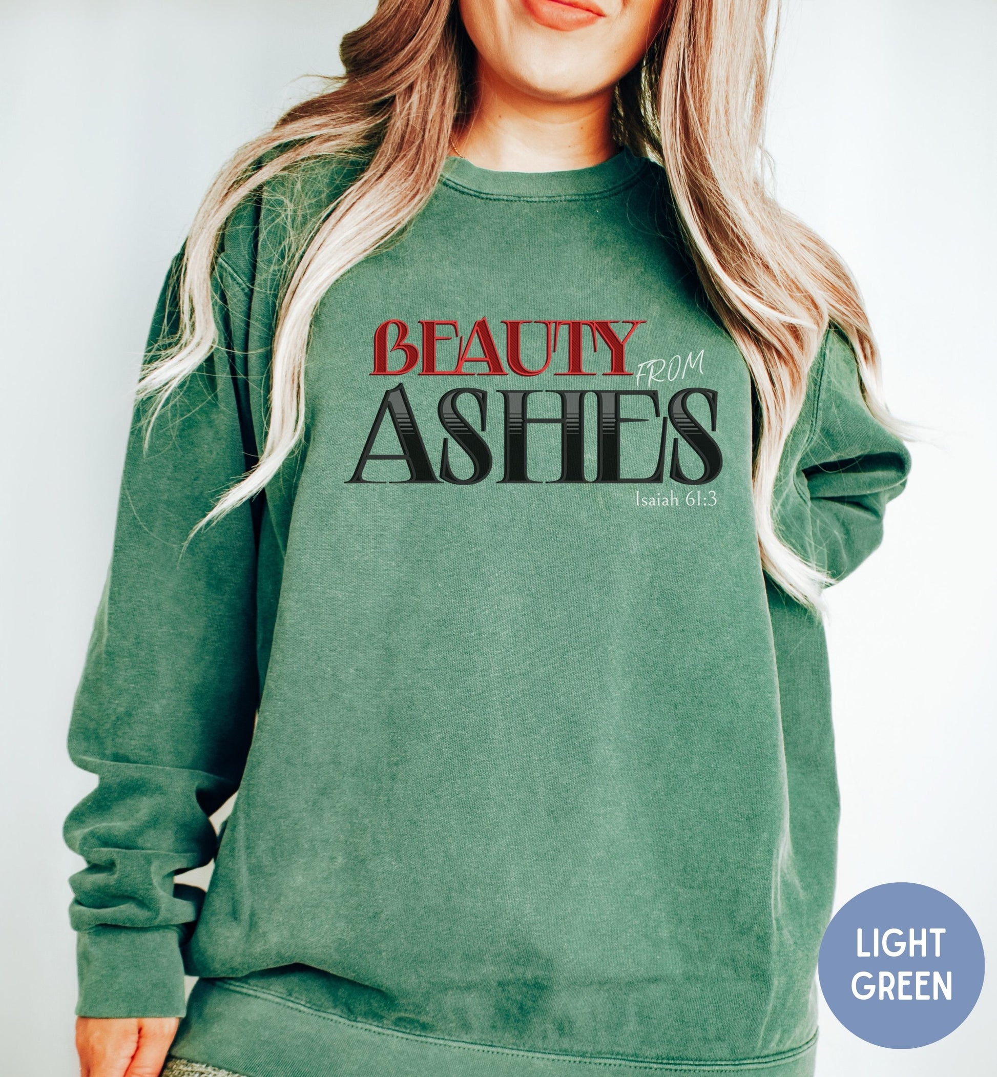 a woman wearing a green sweatshirt with the words beauty from ashes on it